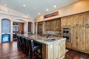 Kitchen featuring lofted ceiling, a spacious island, a kitchen breakfast bar, stainless steel appliances, and light stone counters