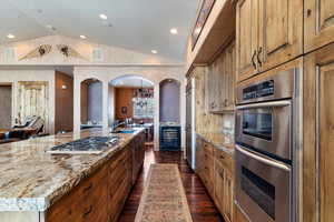 Kitchen featuring stainless steel appliances, wine cooler, a large island, vaulted ceiling, and light stone counters