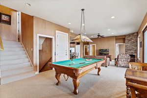 Game room featuring light carpet, a fireplace, billiards, wood walls, and ceiling fan