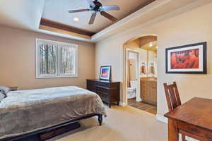 Carpeted bedroom with ceiling fan, a raised ceiling, and ensuite bath