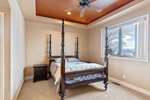 Carpeted bedroom featuring a raised ceiling and ceiling fan