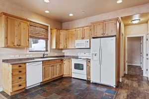 Kitchen with light brown cabinetry, sink, and white appliances