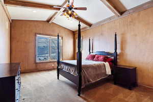 Carpeted bedroom with ceiling fan and vaulted ceiling with beams