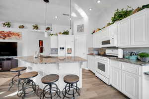 Kitchen with decorative light fixtures, white cabinetry, white appliances, and a kitchen island with sink