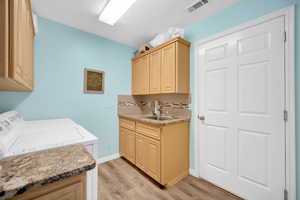 Laundry room featuring light wood-type flooring, cabinets, washer and clothes dryer, and sink