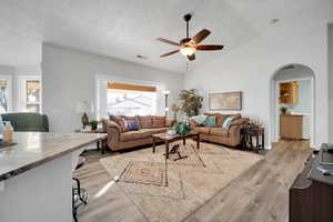 Living room with ceiling fan, a textured ceiling, vaulted ceiling, and light wood-type flooring