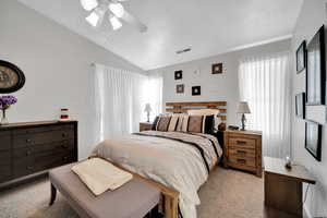 Carpeted bedroom featuring ceiling fan, multiple windows, and lofted ceiling