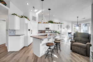 Kitchen with decorative light fixtures, backsplash, a center island with sink, white appliances, and light stone counters