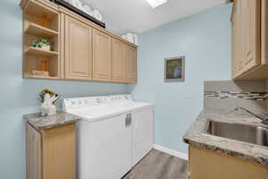 Laundry area featuring washer and clothes dryer, sink, light hardwood / wood-style floors, and cabinets