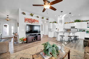 Living room featuring light wood-type flooring, ceiling fan with notable chandelier, a high ceiling, and sink