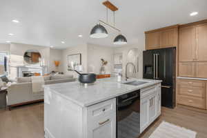 Kitchen featuring black appliances, white cabinetry, an island with sink, sink, and hanging light fixtures