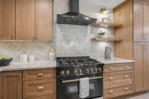 Kitchen featuring light stone counters, tasteful backsplash, exhaust hood, and gas stove