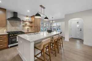 Kitchen with range with gas cooktop, a kitchen island with sink, a kitchen breakfast bar, wall chimney exhaust hood, and sink