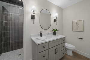 Bathroom featuring toilet, a tile shower, wood-type flooring, and vanity