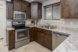 Kitchen featuring appliances with stainless steel finishes, light stone counters, dark brown cabinetry, and sink