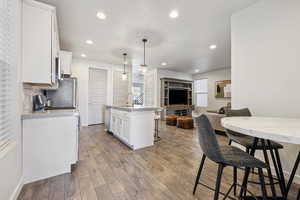 Kitchen featuring hardwood / wood-style flooring, a breakfast bar, stainless steel appliances, white cabinetry, and backsplash