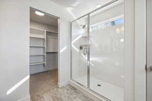 Full bathroom featuring a shower stall, a spacious closet, and baseboards