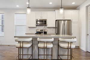 Kitchen with dark wood-style floors, a center island with sink, stainless steel appliances, decorative backsplash, and a sink
