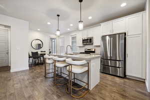 Kitchen with dark wood-style floors, appliances with stainless steel finishes, a center island with sink, and decorative backsplash