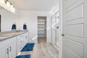 Full bath with double vanity, a shower stall, a spacious closet, and a sink