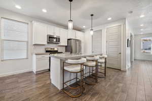Kitchen with tasteful backsplash, a center island with sink, dark wood finished floors, stainless steel appliances, and white cabinetry