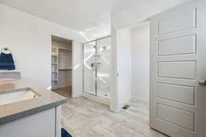 Bathroom featuring marble finish floor, double vanity, visible vents, a spacious closet, and a stall shower