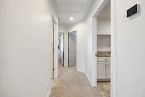 Corridor with attic access, baseboards, and light colored carpet