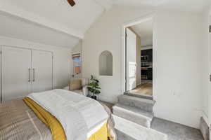 Carpeted bedroom featuring ceiling fan, a closet, and vaulted ceiling with beams