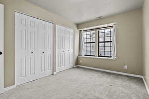 Unfurnished bedroom with light carpet, multiple closets, and a textured ceiling