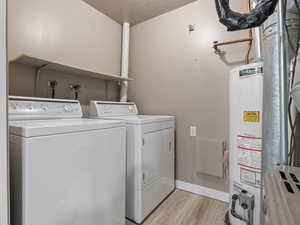 Clothes washing area with water heater, separate washer and dryer, a textured ceiling, and light hardwood / wood-style floors