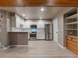 Kitchen featuring white cabinetry, stainless steel appliances, tasteful backsplash, light wood-type flooring, and light stone counters