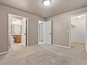 Unfurnished bedroom with ensuite bathroom, a walk in closet, a closet, and light carpet