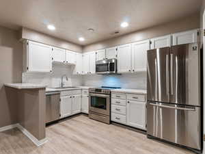 Kitchen featuring white cabinets, backsplash, sink, and stainless steel appliances