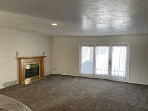 Unfurnished living room with dark colored carpet, a tile fireplace, and a textured ceiling