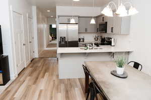 Kitchen with hanging light fixtures, sink, gray cabinetry, a breakfast bar area, and stainless steel appliances