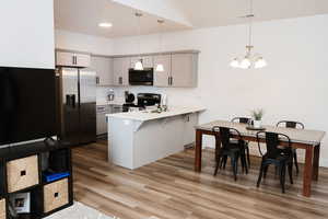 Kitchen featuring appliances with stainless steel finishes, gray cabinetry, decorative light fixtures, kitchen peninsula, and a breakfast bar area