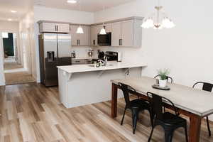 Kitchen with pendant lighting, a kitchen bar, stainless steel appliances, kitchen peninsula, and gray cabinetry