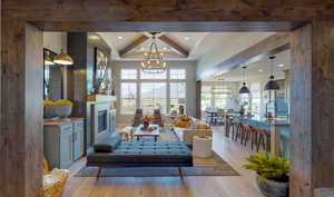 Living room with a notable chandelier, a wealth of natural light, beamed ceiling, and light wood-type flooring