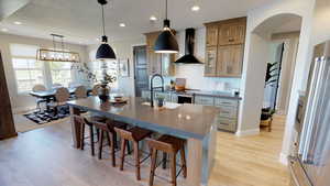 Kitchen with decorative light fixtures, light hardwood / wood-style flooring, wall chimney range hood, a large island, and backsplash