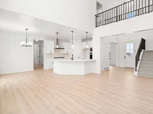 Kitchen featuring white cabinets, backsplash, hanging light fixtures, a kitchen island with sink, and wall chimney range hood