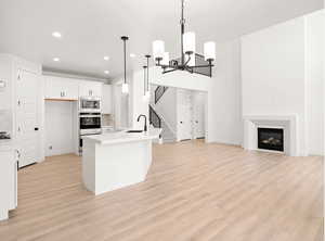 Kitchen with light hardwood / wood-style flooring, stainless steel appliances, decorative backsplash, white cabinets, and decorative light fixtures