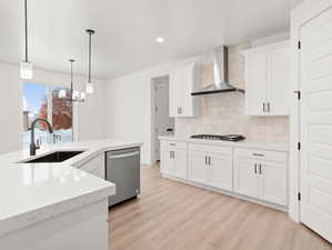 Kitchen with pendant lighting, sink, appliances with stainless steel finishes, white cabinets, and wall chimney exhaust hood