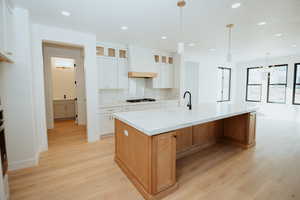 Kitchen with white cabinetry, a large island with sink, hanging light fixtures, custom exhaust hood, and light stone countertops
