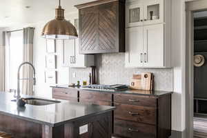 Kitchen with stainless steel gas stovetop, white cabinetry, dark brown cabinets, and sink
