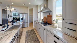 Kitchen with light stone counters, decorative light fixtures, a chandelier, stainless steel appliances, and wall chimney range hood