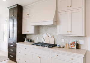 Kitchen with custom exhaust hood, tasteful backsplash, white cabinets, and stainless steel gas stovetop