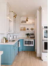 Kitchen with sink, appliances with stainless steel finishes, tasteful backsplash, blue cabinets, and light wood-type flooring