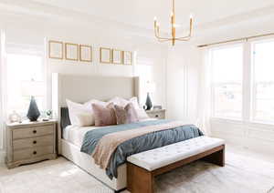Bedroom with light colored carpet, multiple windows, and a notable chandelier