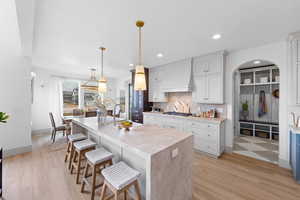 Kitchen featuring stainless steel gas stovetop, backsplash, premium range hood, white cabinets, and decorative light fixtures