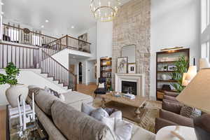 Living room featuring a chandelier, wood-type flooring, a towering ceiling, and a stone fireplace